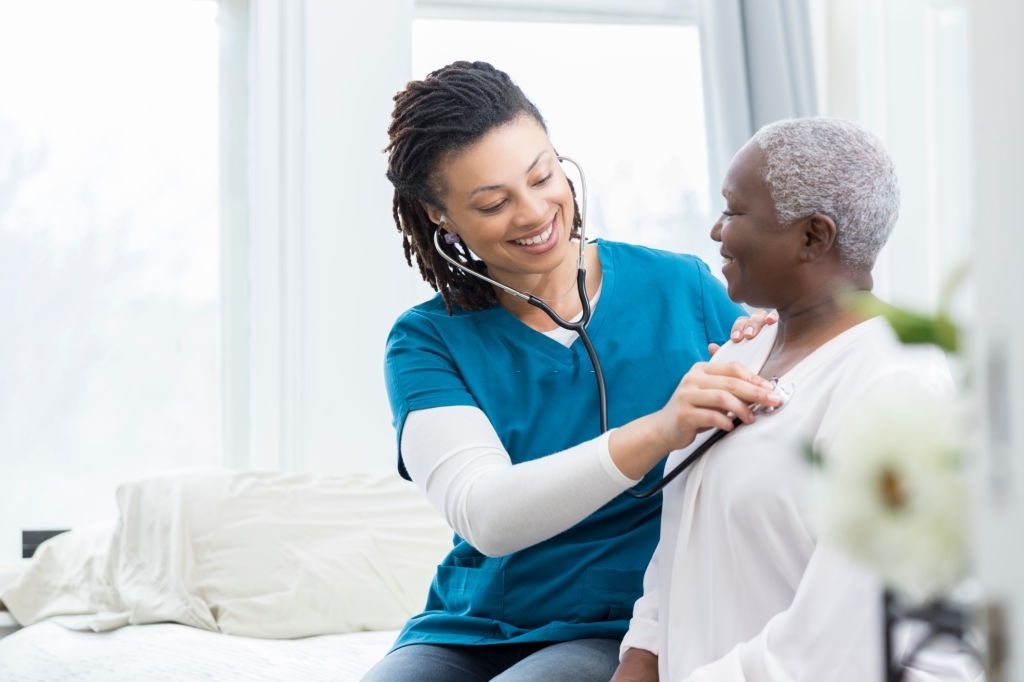 Young African American home healthcare nurse checks a senior female patient's vital signs. The senior woman is recovering at home from a recent surgery.